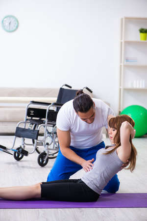The male physiotherapist doing exercises with injured woman on floorの写真素材