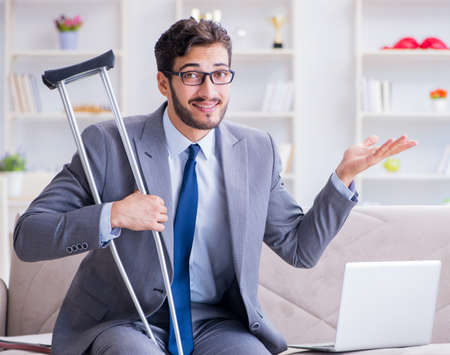 Businessman with crutches and broken leg at home workingの写真素材