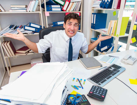 Businessman working in the office with piles of books and papersの写真素材