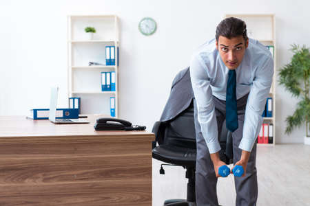 Young handsome employee doing sport exercises at workplaceの写真素材