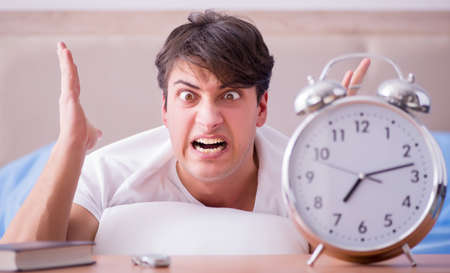 Man in bed frustrated suffering from insomnia with an alarm clocの写真素材