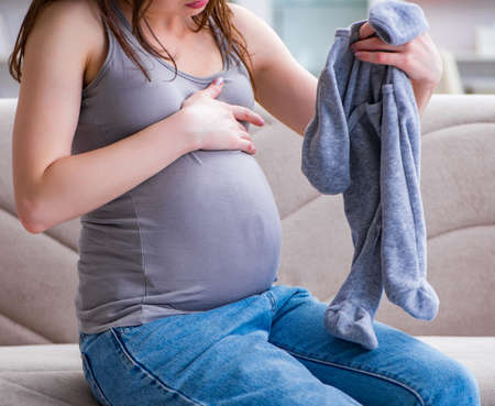 The pregnant woman with a belly tummy sitting on a sofa at homeの写真素材