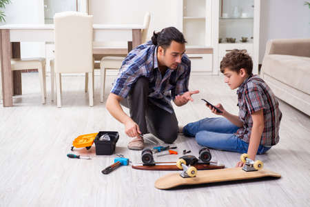 Young father repairing skateboard with his son at homeの写真素材