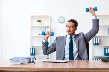 Young handsome employee doing sport exercises at workplaceの写真素材