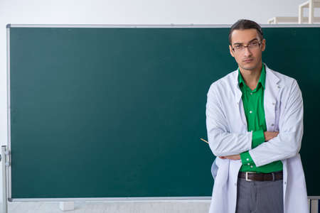 Young male chemist teacher in front of blackboardの写真素材