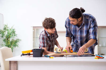 Young father repairing skateboard with his son at homeの写真素材