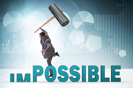 Businessman hitting the word impossible with hammer