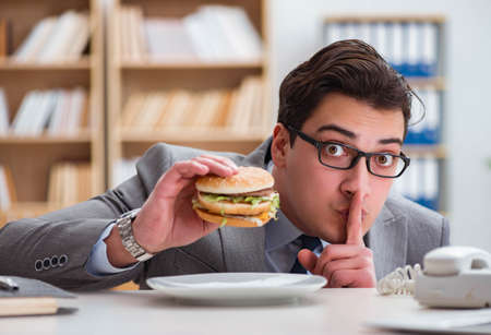 Hungry funny businessman eating junk food sandwichの写真素材