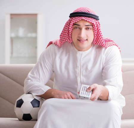 Young arab man watching football sitting on sofaの写真素材