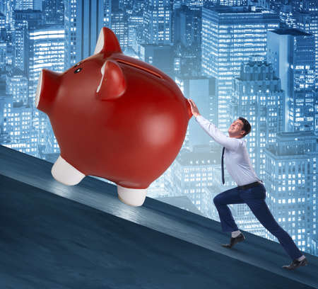 Man pushing piggybank uphill in business conceptの写真素材