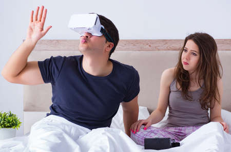 Wife and husband with virtual reality goggles in the bed