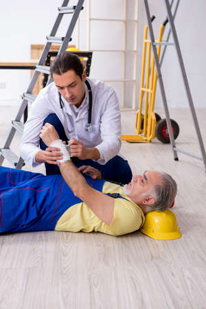 Young male doctor and old contractor in first aid conceptの写真素材