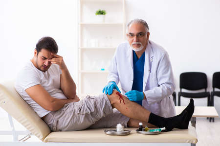 Leg injured man visiting old doctor in first aid conceptの写真素材