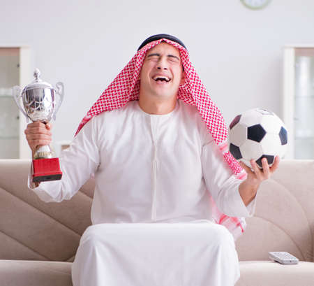 Young arab man watching football sitting on sofaの写真素材