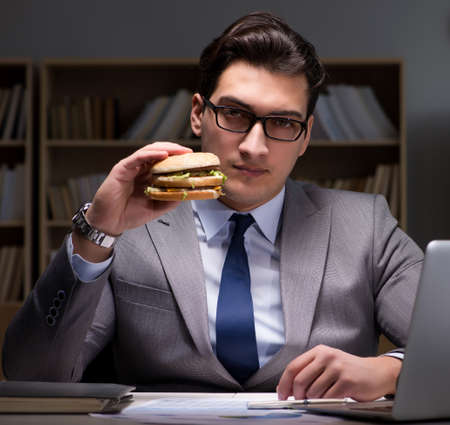 Businessman late at night eating a burgerの写真素材