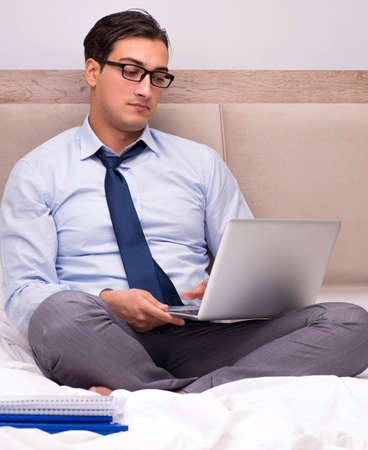 Businessman working in the bed at homeの写真素材