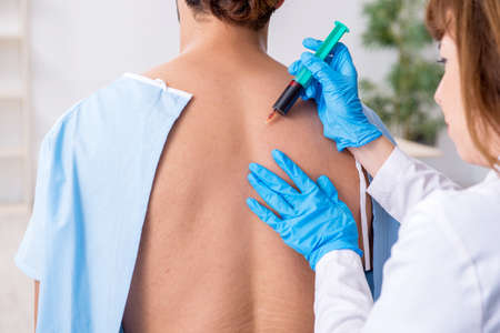 Young back injured man visiting female doctor chiropractor