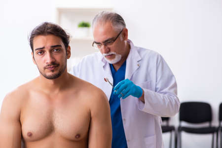 Injured young man visiting experienced male doctorの写真素材