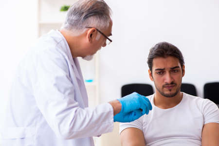 Leg injured man visiting old doctor in first aid conceptの写真素材