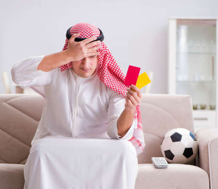 Young arab man watching football sitting on sofaの写真素材