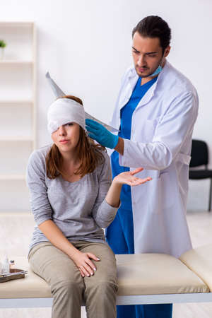 Young head injured woman visiting young male doctorの写真素材