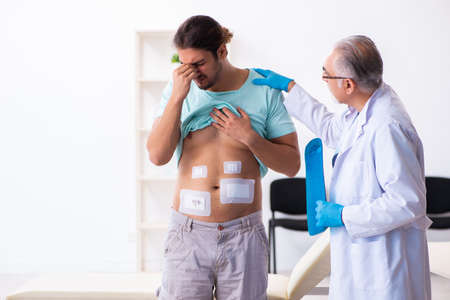 Injured young man visiting experienced male doctorの写真素材