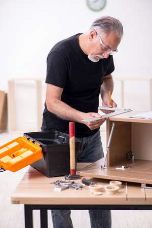 Old carpenter working indoors on furnitureの写真素材