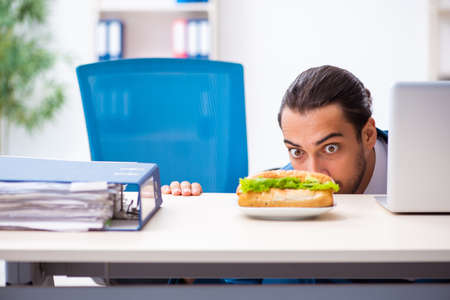 Young male employee having breakfast at workplaceの写真素材