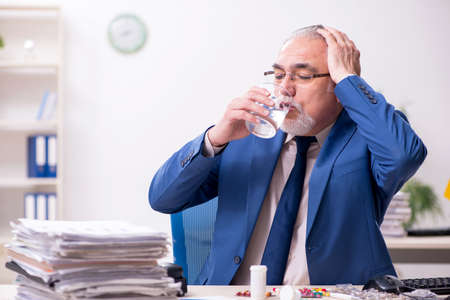 Old male sick employee working overtime in the officeの写真素材