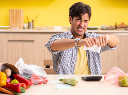 Young man calculating expences for vegetables in kitchenの写真素材