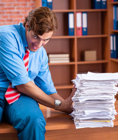 Young employee with excessive work sitting at the officeの写真素材
