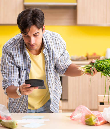 Young man calculating expences for vegetables in kitchenの写真素材