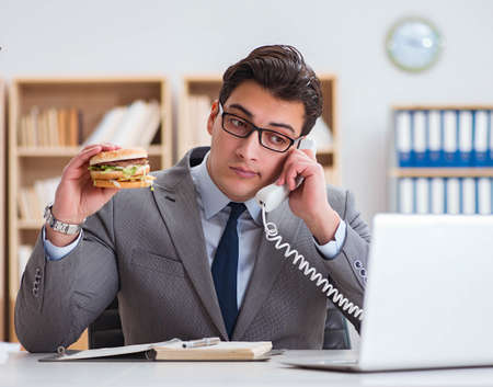 Hungry funny businessman eating junk food sandwichの写真素材