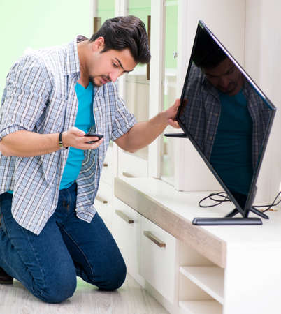 Young man husband repairing tv at homeの写真素材