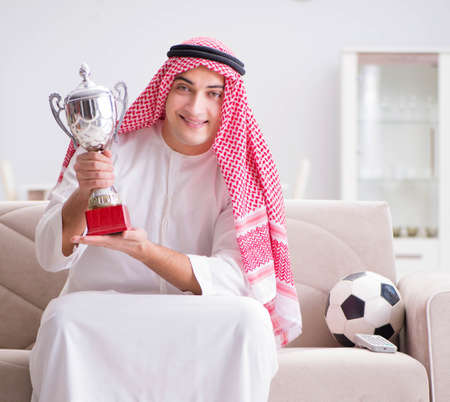 Young arab man watching football sitting on sofa