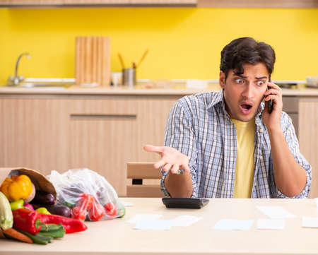 Young man calculating expences for vegetables in kitchenの写真素材