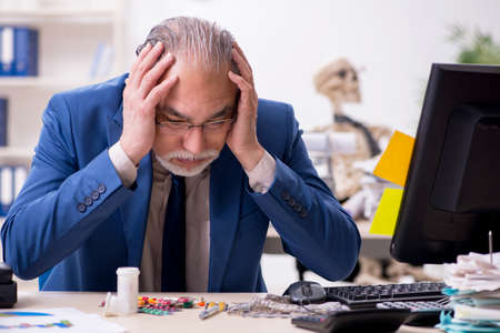 Old male sick employee working overtime in the officeの写真素材