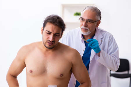 Injured young man visiting experienced male doctorの写真素材