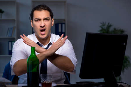 Alcohol addicted businessman working late in the officeの写真素材