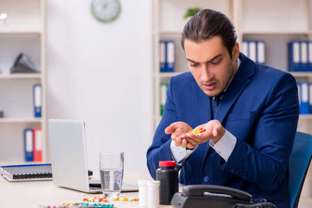 Young male employee and a lot of pills on the deskの写真素材