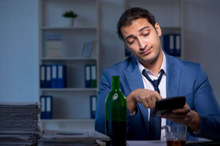 Alcohol addicted businessman working late in the officeの写真素材