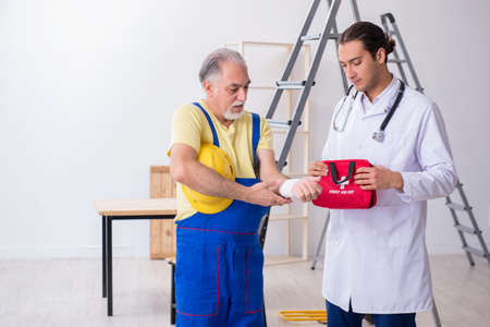 Young male doctor and old contractor in first aid conceptの写真素材