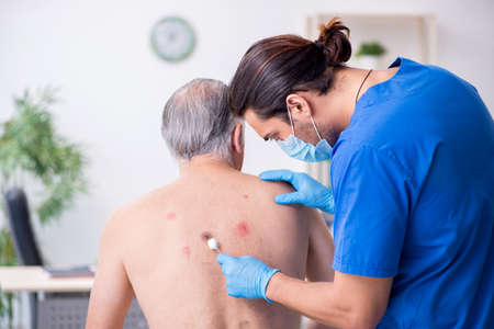 Old man visiting young male doctor dermatologistの写真素材