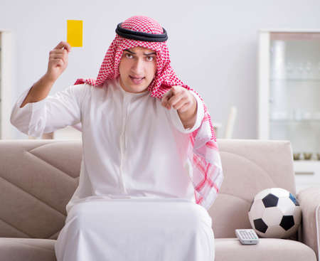 Young arab man watching football sitting on sofaの写真素材