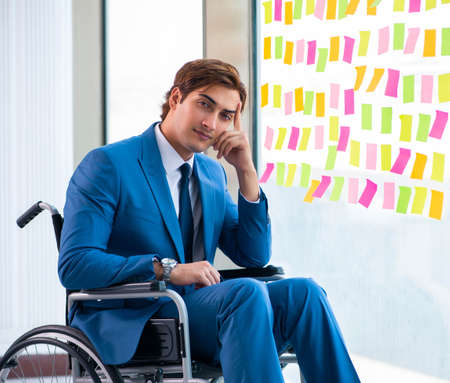 Young handsome man in wheelchair with many conflicting prioritieの写真素材
