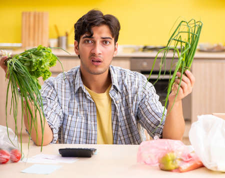 Young man calculating expences for vegetables in kitchenの写真素材