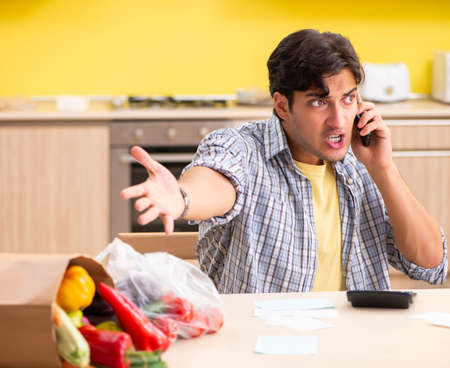 Young man calculating expences for vegetables in kitchenの写真素材