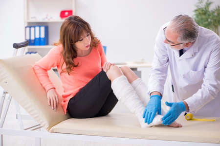 Young leg injured woman visiting old doctor traumatologistの写真素材
