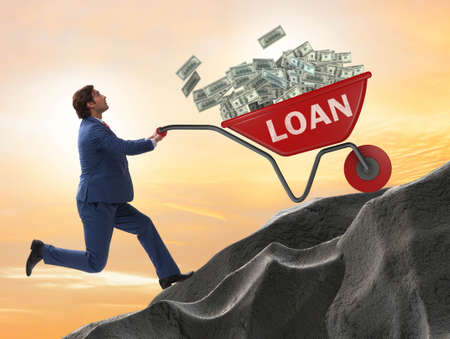 Businessman pushing wheelbarrow uphill in debt loan conceptの写真素材