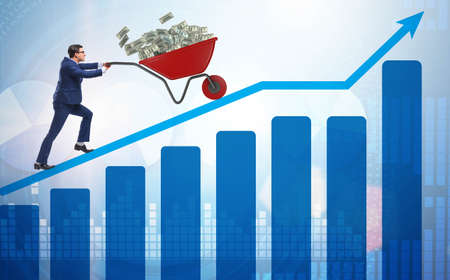 The businessman pushing wheelbarrow full of dollar moneyの写真素材